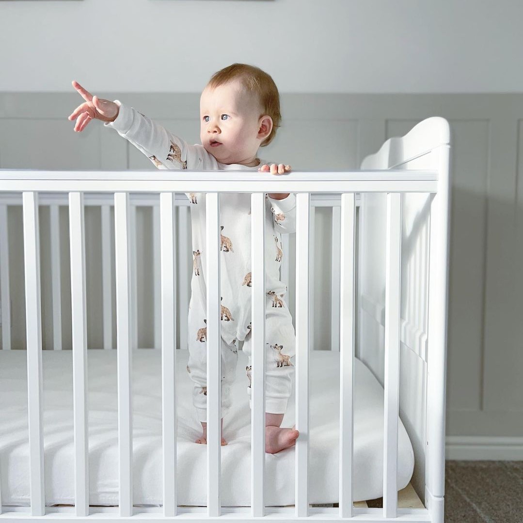 Baby stood in a cot pointing